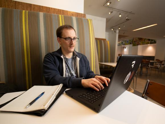 Master of Public Administration student working on a laptop in a campus building.