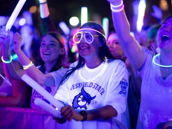 Students hold glow sticks and wear glowing necklaces and glasses while dancing