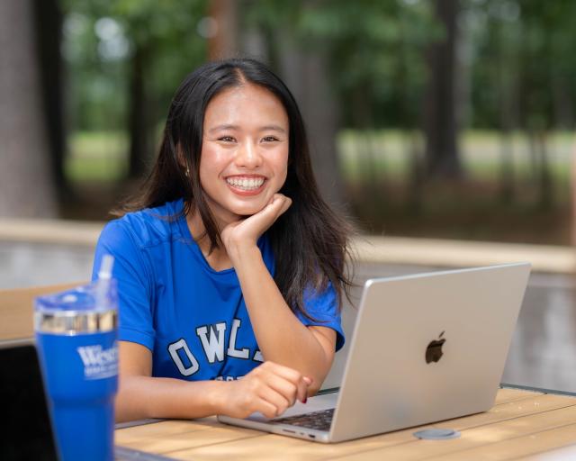 Student smiling outdoors while working on a laptop.
